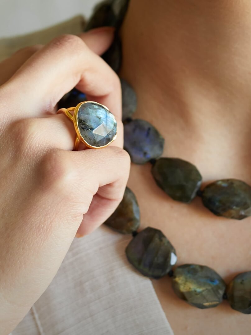 A woman's hand adorned with a gold ring featuring a mesmerizing labradorite stone.